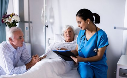 A woman in a hospital bed with a man sitting bedside and a doctor sitting on the bed.